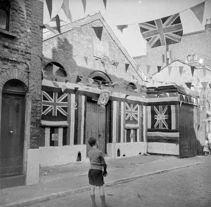 black and white photograph of a boy in a street covered with bunting, for Queen Elizabeth's coronation in 1953