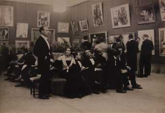 A group of people in evening dress sit in an exhibition space