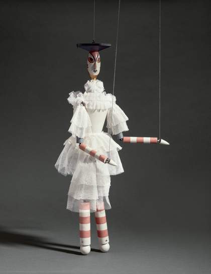 A marionette with stripey arms and legs and a white ruffled dress