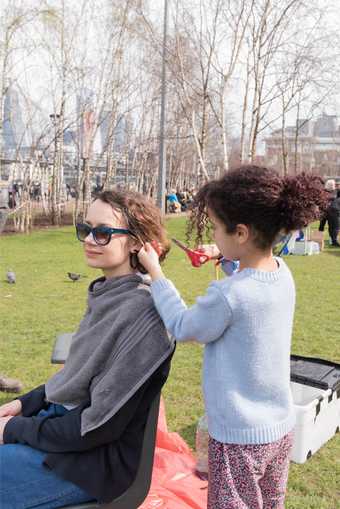young girl cutting the hair of a woman in a park