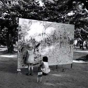 Two children drawing on a big wooden board in a park