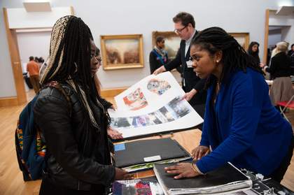 An adult giving a student advice on their art portfolio in a gallery