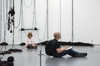 Two people sit sketching in a gallery space