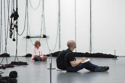 Two people sit sketching in a gallery space