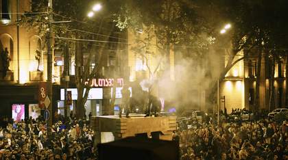 a hazy scene of a select number of protestors on a platform amidst a large rally