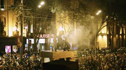 a hazy scene of a select number of protestors on a platform amidst a large rally