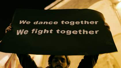 A young protestor holds up a sign that reads 'We dance together / We fight together'