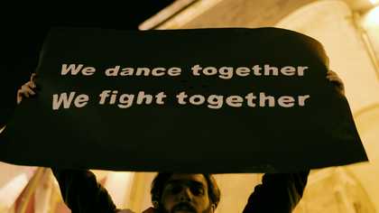 A young protestor holds up a sign that reads 'We dance together / We fight together'