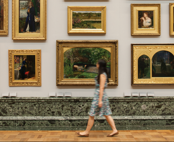 A woman walks through the 1840 gallery with paintings in the background