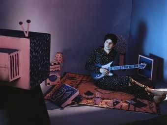 Artist Jerkcurb sitting on a bed with a guitar