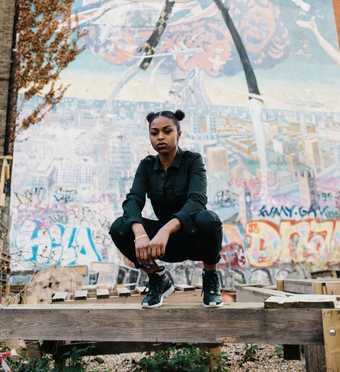 Artist Nadia Rose squatting on a gate