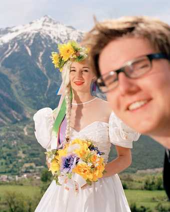 A colour photograph of woman in a wedding dress appears against a mountain background with a person photobombing in front