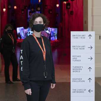 a visitor assistant stands with some signs showing the one way routes in the galleries 
