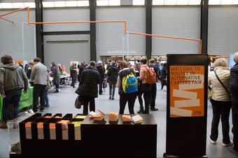 A crowd of people at the Routes In Alternative Careers Fair in the Turbine Hall at Tate Modern, with a welcome sign in the foreground bearing the name of the event
