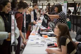 Young people smiling, talking and sharing materials across a long table at the Alternative Careers Fair