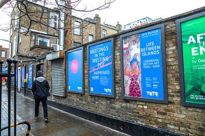 Four billboard posters evenly spaced along a wall a person walking by