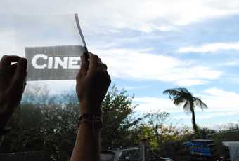 Runa Islam still from CINEMATOGRAPHY image of a pair of hands holding up a transparency to the sky with the text cine