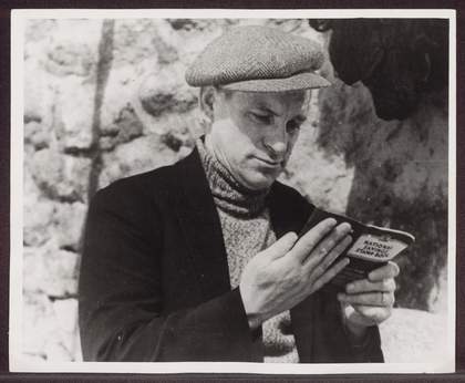 Black and white photograph of a person wearing a flat cap reading a book.