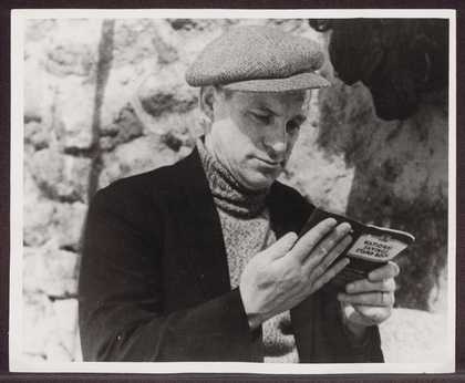 Black and white photograph of a person wearing a flat cap reading a book.