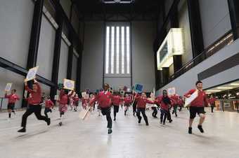 Children in school uniform run in turbine hall with placards
