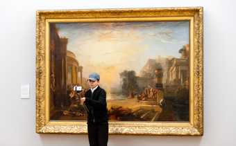 Young person using a selfie stick in front of an artwork