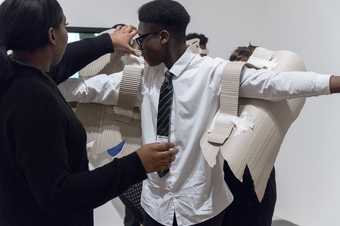 Photograph of students collaborating making cardboard wings, putting them on the back of another student during a workshop at Tate Modern