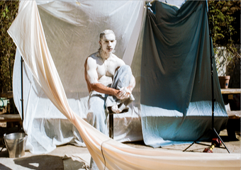 Photo of a man in white clay surrounded my hanging sheets
