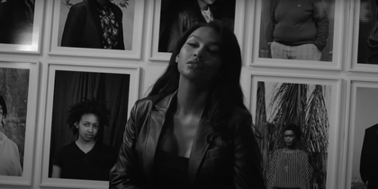 Black and white image of Lili St Jerry posing in front of artworks of Zanele Muholi