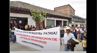 Protestors marching in the street holding up a banner - the text begins: ALTO A LA VENTA DE NUESTRA PATRIA!