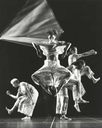 Black-and-white photograph depicting four figures creating different shapes with their bodies in a dark interior