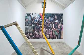 A large photograph on the back wall of the gallery is obscured by coloured wooden pieces of wood stretching from floor to ceiling.