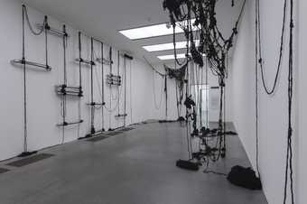 Installation shot showing strings of black human hair draping from the walls and ceiling in a gallery space at Tate Modern