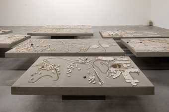 A series of lying grey tables with clay shapes placed on them.