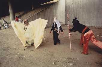still from film showing three people in big costumes posing in derelict concrete area
