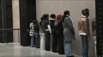 Still image from video footage of Group of persons facing a wall performance