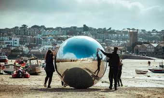 People roll a large silver ball on St Ives' Harbour Beach