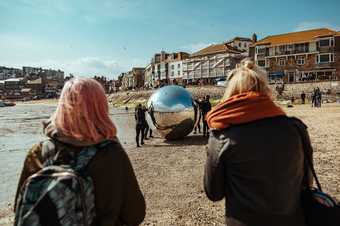 Two people watch as a large silver ball is moved across the sand at St Ives' Harbour beach