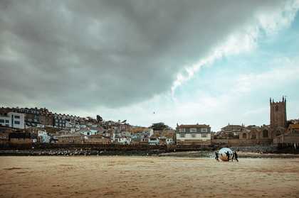 People run with a giant silver ball as some gulls fly