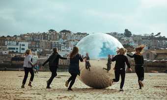 People chase a large, silver ball across the sand of St Ives' Harbour Beach