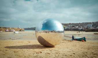 Photograph of the large silver ball from special performance 063 Urban Songline (Another Hurling of the Silver Ball) by Allard Van Hoorn sits on St Ives' Harbour Beach