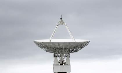 a big satellite dish with a grey cloudy sky behind it