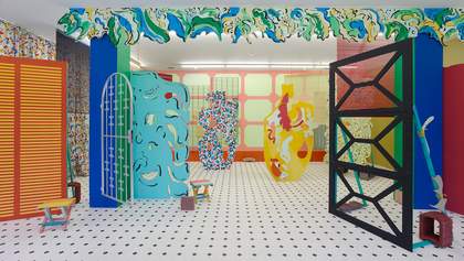 A room with a white floor with black dots, filled with brightly coloured sculptures and artworks made to look like ornaments and furnishings