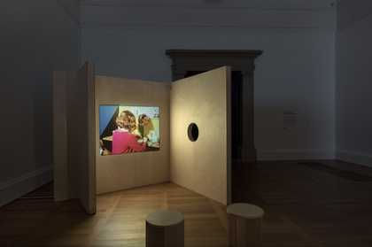 photograph of the exhibition. plywood structures small stools and a film projected onto the wall