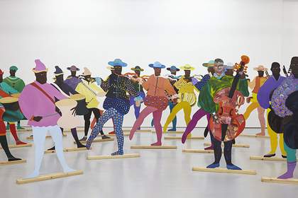 A group of 2D cut-out Black figures appear in colourful dress spaced out across a gallery