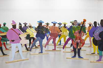 A group of 2D cut-out Black figures appear in colourful dress spaced out across a gallery