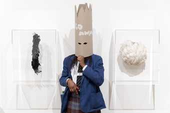 A student in a mask beside two mask artworks