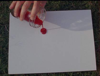 a hand over a blank paper poring a red liquid