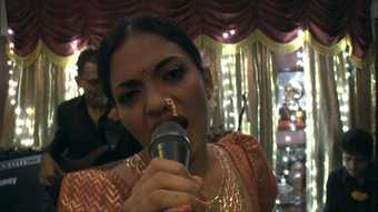 Film still of an indian woman singing into a microphone in a karaoke bar