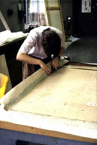 A conservator attaches a strip-lining to the edges of a canvas
