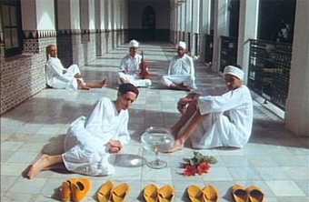 photograph of five men in traditional white clothing, sitting on a floor in Tangier. Orange shoes are laid out in front of them.